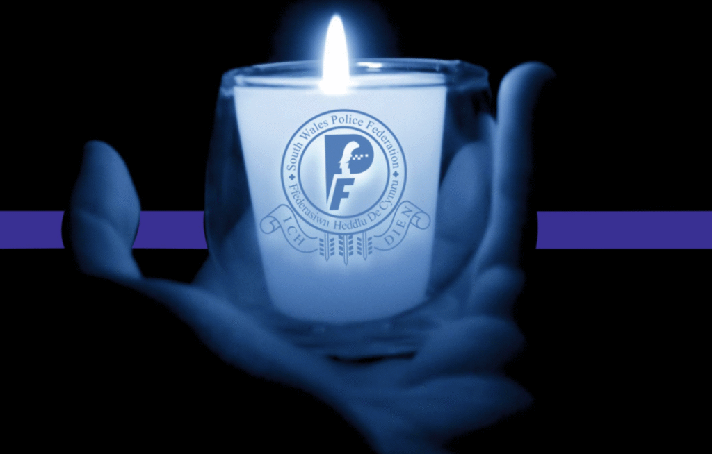 A hand holds a candle with an open flame. Written on the candle holder is the South Wales Police Federation logo