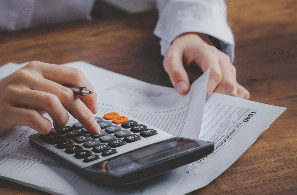 A man types into a calculator while holding some papers