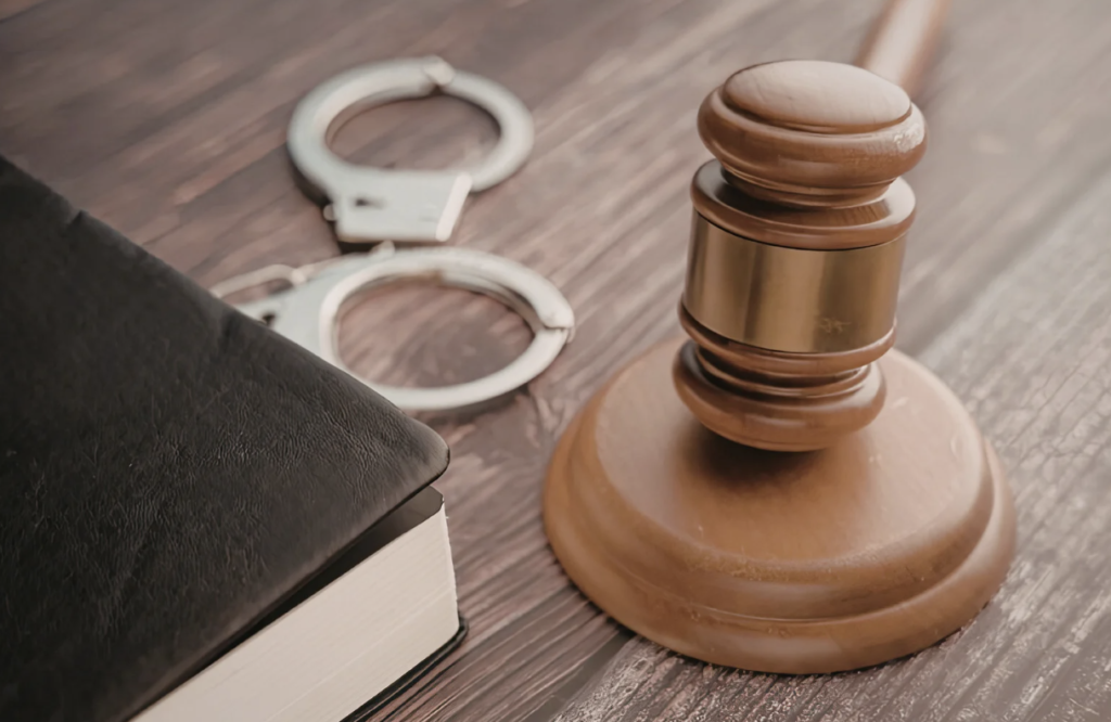 A legal hammer hits a desk with a pair of handcuffs also on the desk.