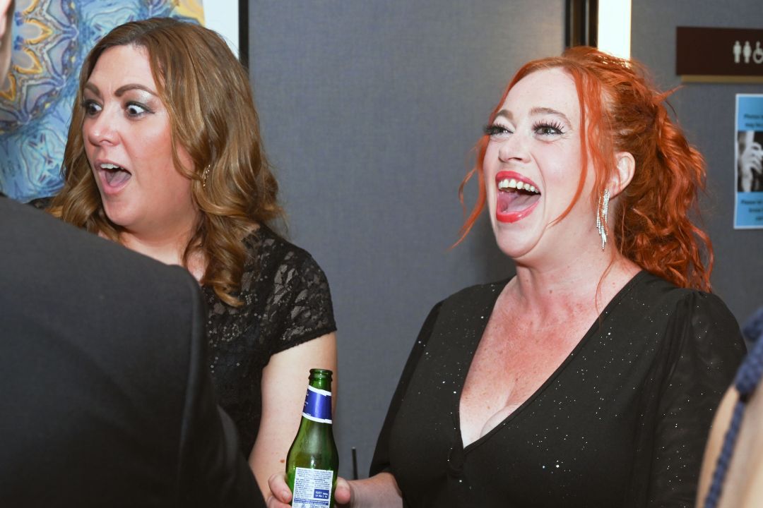 A lady with red hairs laughs out loud while a lady with brown hair looks shocked in jest at the blue heart ball
